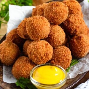 A pile of Bitterballen on a tray with mustard in front of them.