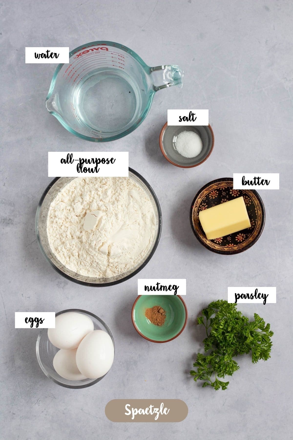 Ingredients for homemade German spaetzle, including flour, eggs, water, salt, butter, nutmeg, and parsley.