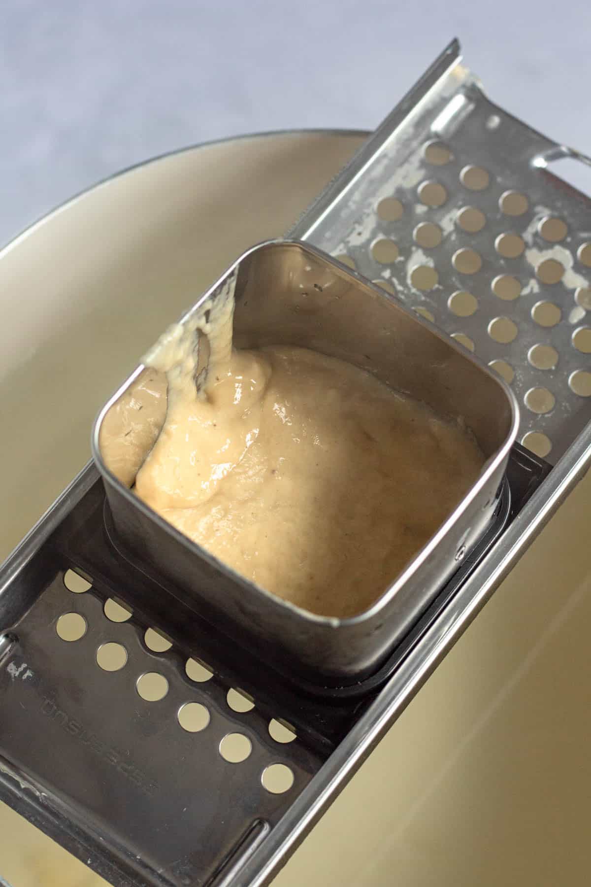 Spaetzle batter being pressed through a spaetzle maker into boiling water.